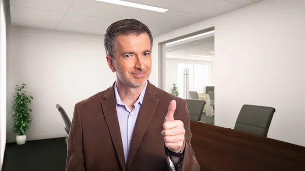 一个白发苍苍的中年商人 穿着一件棕色的夹克站在办公室里 描述初创公司和企业业务 他大拇指表示赞同 — 图库照片