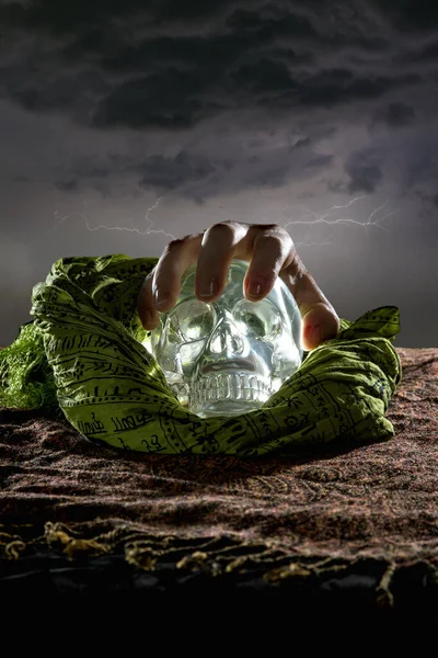 Hand grabbing a scary or creepy glowing crystal skull on Halloween holiday or Dia De Los Muertos Day of the Dead festival.  Depicts horror theme and superstition.