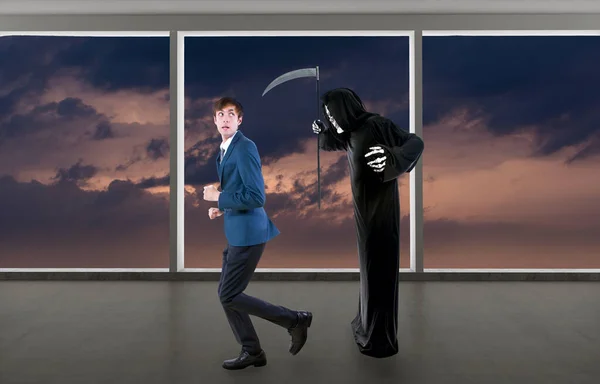 Man in a Halloween grim reaper ghost costume chasing, mocking and making fun of scared businessman running away.  Can also depict death following a man as a metaphor for life insurance.