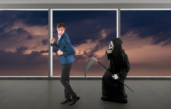 Man in a Halloween grim reaper ghost costume chasing, mocking and making fun of scared businessman running away.  Can also depict death following a man as a metaphor for life insurance.