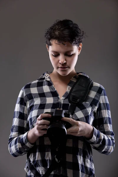 年轻的女摄影师在工作室里拿着相机 她的姿势和照明 以便背景可以改变为复合材料 在灰色背景下拍摄 — 图库照片