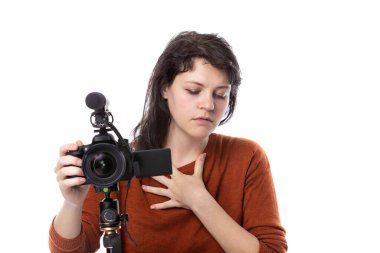 Kamera ve mikrofonu olan genç bir kadın ya da beyaz arka planda online içerik yaratıcısı. Sinema öğrencisi ya da hasta görünümlü serbest çalışan birine benziyor.  