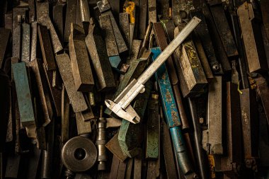 Metal fabrikasının atölyesinde paslı çelik aletler ve kalibreler masanın üstünde.