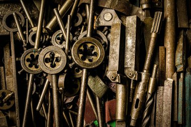 Metal fabrikasının atölyesindeki masada paslı çelik aletler ve iplikler var.