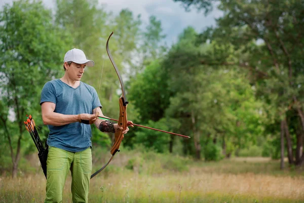 El hombre está con el bosque y sostiene un arco deportivo. carga la flecha . —  Fotos de Stock