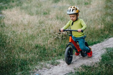 Boy todler rides a treadmill on the track in the summer. he has a helmet on his head and a shoe protection on his feet. 