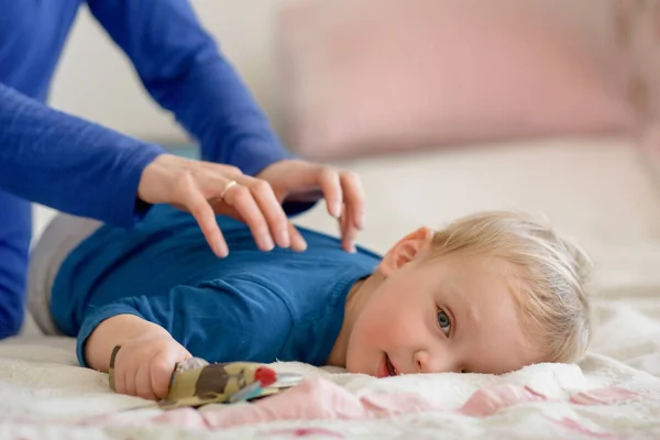 The baby calmly lies on the bed and he is massaged on his back. The girls hands are visible in the frame. — ストック写真