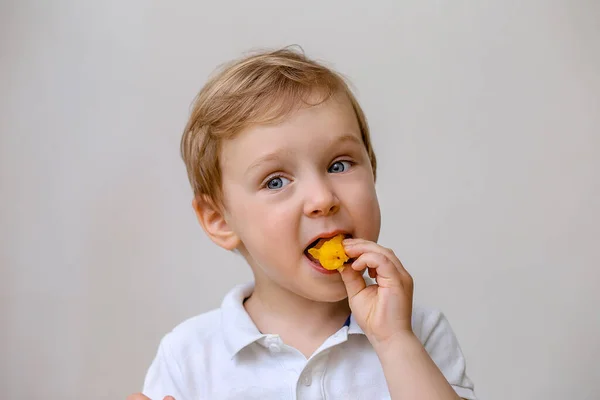 Um todler menino leve come uma fruta laranja . — Fotografia de Stock