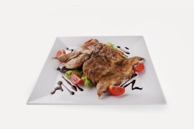 Grilled quail is laid out on a white plate. The dish is decorated with sauce and tomatoes.