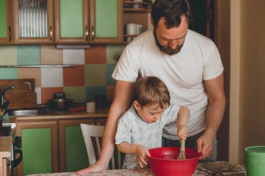 Üç yaşında bir çocuk mutfakta bir turta hazırlıyor. Baba çocuğun yemek yapmasına yardım eder. Küçük çocuk çırpıcıyla karıştırır kaseyi
