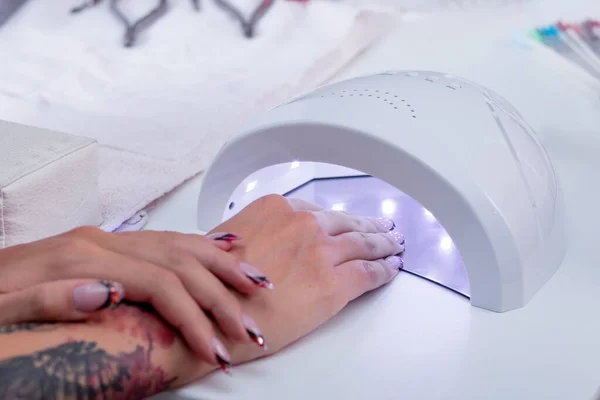 Womens manicured hands with a new manicure while drying the varnish gel in an ultraviolet LED lamp — Stock Photo, Image
