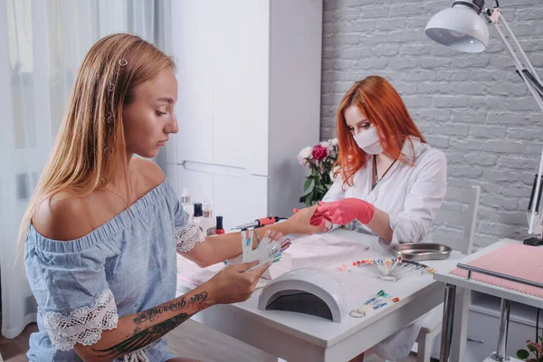 The girl with the tattoo chooses the color of the varnish while the master does her manicure on her hands. — Stock Photo, Image