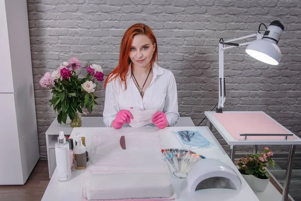 Red-haired girl manicure master sits in the office at the table and waits for his client. — Stock Photo, Image