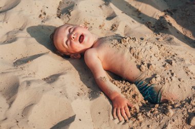 Küçük çocuk kumsalda eğleniyor ve kumsalda yatıyor.