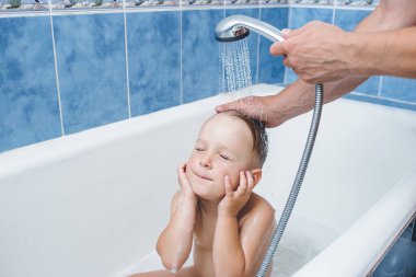 Şirin bir çocuk küvette köpükle banyo yapıyor. Gözlerini ve kulaklarını kapattı. Babacık bebek kafası yıkıyor. 