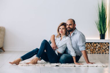 Sakallı bir adam ve bir kadın, Von beyaz duvarın üzerinde, bir ışık odasında, yerde ve ahşap iç döşemede oturuyor.