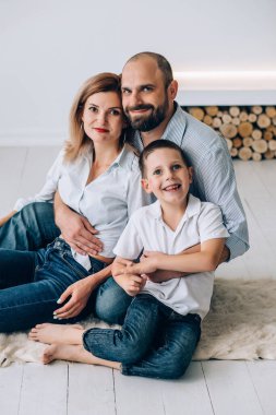 Aile, beyaz zeminde bir odada oturuyor ve kahkahalarla gülüyor. Anne, baba ve genç oğul yerde kucaklaşıyorlar.