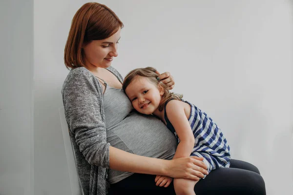 Barn flicka sitter på benen av en gravid mor och kommunicera med barnet i kvinnans mage Stockbild