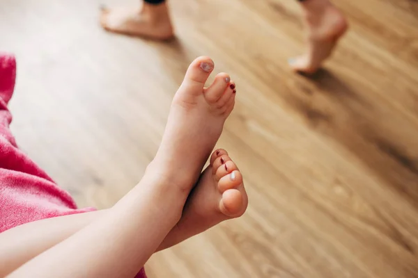 Gambe per bambini con unghie dipinte su uno sfondo di parquet marrone. Immagini Stock Royalty Free