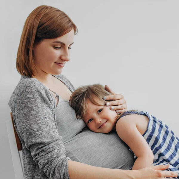 Barn flicka sitter på benen av en gravid mor och kommunicera med barnet i kvinnans mage Stockbild