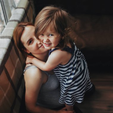 Küçük kız annesine nazikçe sarılıyor ve kameraya bakıyor. Yukarıdan görüntüle. 