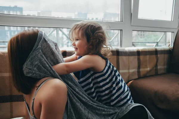 Dziewczyna dziecko rozpieszczanie i zabawy z ciężarną kobietą w domu w pobliżu okna, ona zakrywa twarz z tkaniny, szalik. córka bawi się z mamą Obrazy Stockowe bez tantiem