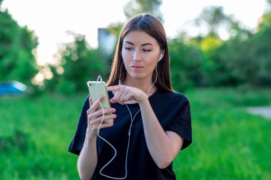Yaz aylarında bir park doğa kız. Bir akıllı telefon kulaklık ile tutar. El parmak bir mesaj çevirir. Yeni bir uygulama açılır. Müzik bir film geri sarar.