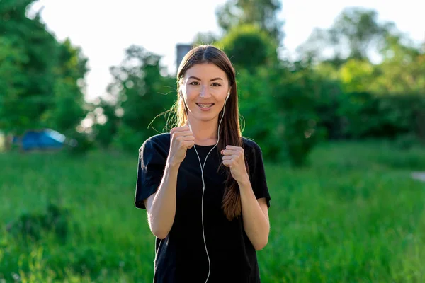 Gadis Asia Brunette. Hal ini berdiri di taman di musim panas pada hari yang cerah. Senyum di gigi kawat gigi. Mendengarkan musik siap untuk pertempuran. Emosi serangan perlindungan dari penjahat . — Stok Foto