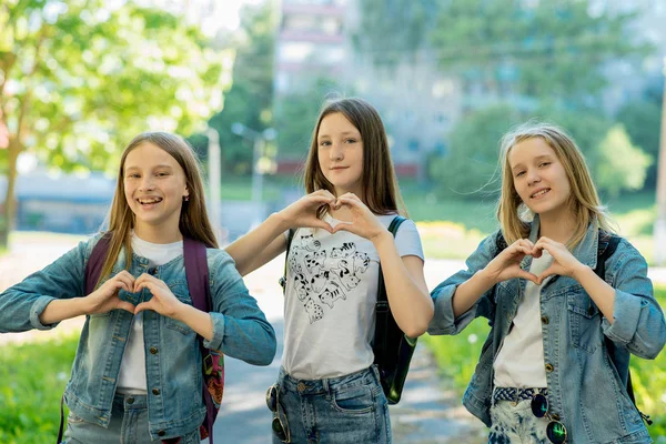 Chicas adolescentes en verano en el parque al aire libre. Las manos del gesto muestran el corazón del amor. Vestido con ropa casual. Los mejores amigos de la novia adolescente. Descanso después de la escuela . — Foto de Stock