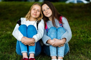 İki genç kız. Doğa yazın. Onlar çim üzerinde oturuyorlar. Birbirleri ile iletişim. Kameraya poz vermek. En iyi dostlar. Yetişkin gelen Gizlilik.