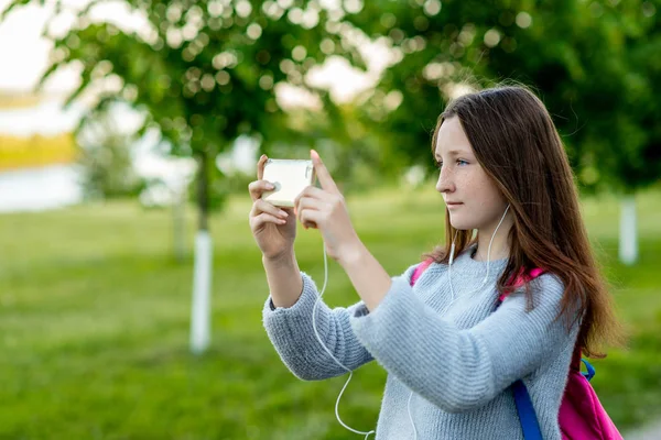 Krásná brunetka. Léto v přírodě. Má smartphone. Je fotografie. Poslouchá hudbu kouká na film. Komunikuje v sociálních sítích. — Stock fotografie