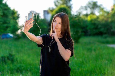 Mutlu yaz aylarında parkta gülümseyen genç esmer kadın. Sosyal ağlarda iletişim kurar. Dudaklarını bir işaret gösteren holding eller demek değildir. Sessizce sessiz olun. Video aramasý duygusal iletişim.