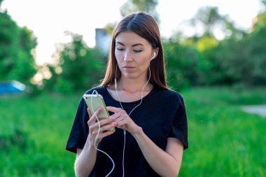 Parkta güzel esmer kız yaz aylarında. Doğada şehir dışında. Telefon ellerini tutar. Kulaklığımda dinler. İletileri sosyal ağlar üzerinde yazar. Belgili tanımlık smartphone üzerinde bir film izlerken.