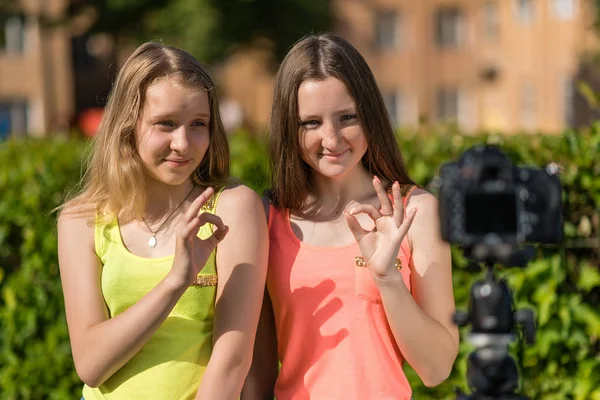 Deux filles en été dans le parc. Jeunes copines blogueuses montrant des gestes de mains OK. Émotionnellement Diffusion vidéo en ligne.Enregistrer vlog et les abonnés au blog. Enregistrer une leçon vidéo pour Internet . — Photo