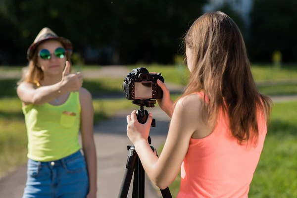 Zwei Freundinnen. Sommer in der Natur. zeigt die Geste des Daumens nach oben. ein sonniger Tag. Record Vlog und Blog-Abonnenten. Video-Unterricht für das Internet aufnehmen. Kamera mit Stativ verwenden. — Stockfoto