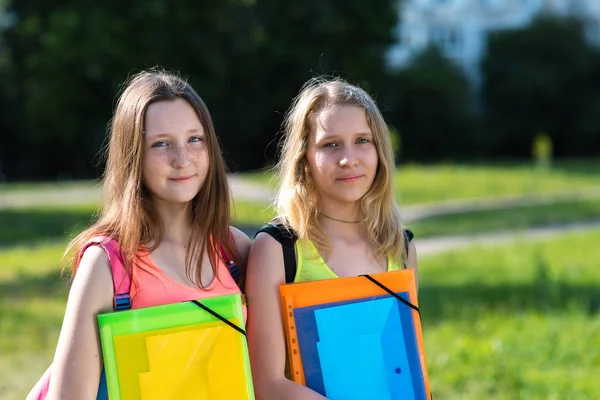 Dwie dziewczyny uczennica. Lato w przyrodzie. Zmęczony studiowania. Nie ma siły, aby dowiedzieć się więcej. W rękach folderu z notebookami. Opiera się on po szkole. Najlepsze dziewczyny. — Zdjęcie stockowe