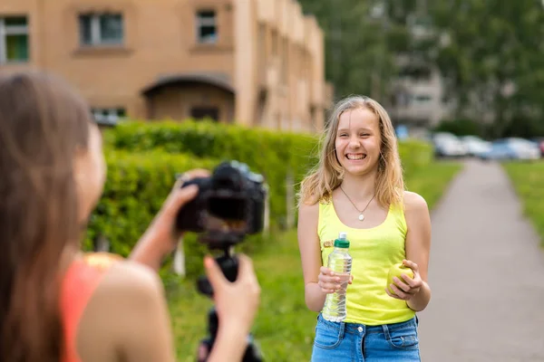 Pour la étudiante. Ecrit la vidéo à la caméra. Dans les mains tenant une pomme dans une bouteille d'eau. Notez un vlog et un blog sur la nutrition correcte. Joyeux sourire. Rire dans la nature . — Photo