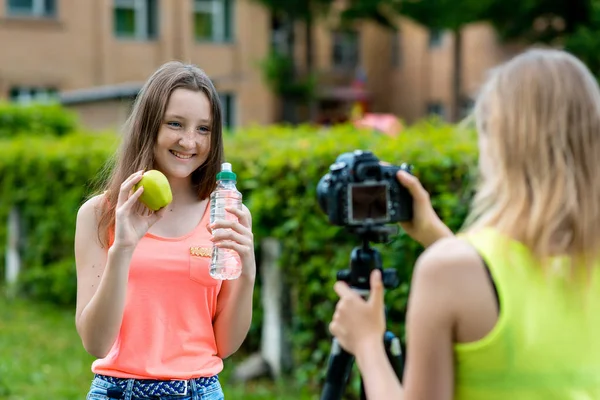 Две девушки летом на природе. Они говорят о здоровом питании. В руках яблока бутылка воды. Счастливо улыбается. Запись vlog и блог подписчиков. Видеозапись уроков для Интернета . — стоковое фото