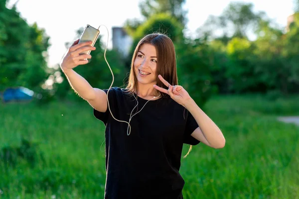 Happy Asian girl smiling at the camera. To call by video call. Speaks on the phone listening to music. Hand gestures. Hello. Summer in field on a green meadow. He speaks in social networks.
