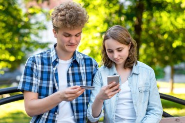 Park Yaz aylarında bir kızla bir adam gibi. Elinde bir smartphone ve bir kredi kartı tutar. İnternette alışveriş yapmak için gülümseyen mutlu.