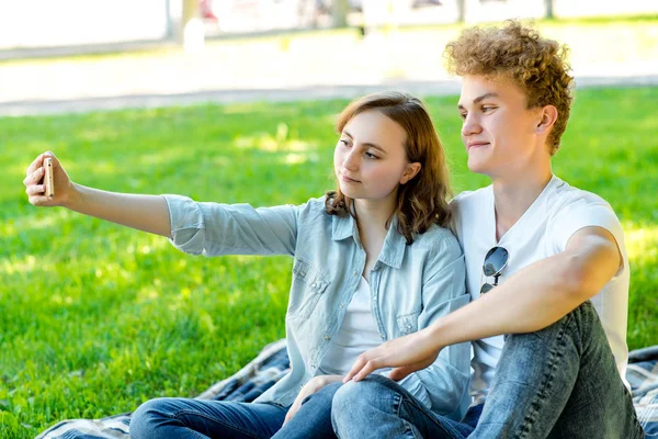 Avec une fille en été dans la nature. Ils sont assis sur une couverture. Il prend des photos de lui au téléphone. Fais un sourire heureux. Les écoliers se reposent dans le parc . — Photo