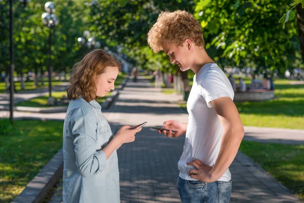 Мальчик и девочка смотрят друг на друга. Лето на природе. В его руках смартфон. Записывает номер телефона. Эмоции, встречающиеся в парке. Концепция знакомств в природе . — стоковое фото