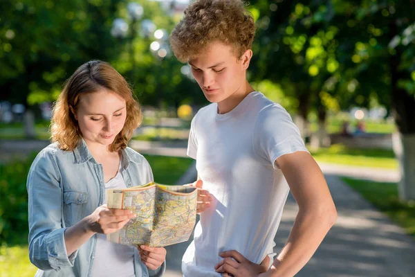 Ein Kerl mit einem Mädchen im Sommer in der Natur. im Stadtpark. In seinen Händen hält er einen Fahrplan. glücklich kommuniziert wählen Sie die Richtung des Weges. gekleidet in lässiger Kleidung. — Stockfoto