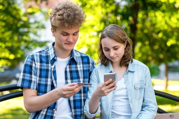 Park Yaz aylarında bir kızla bir adam gibi. Elinde bir smartphone ve bir kredi kartı tutar. İnternette alışveriş yapmak için gülümseyen mutlu.