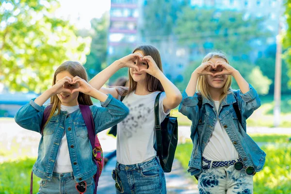 Три дівчинки-підлітки. Літо в природі. Посміхайся щасливо. У стильному джинсовому одязі. Руки жест показує любов. Поняття доброта і позитив. Емоції щастя та дружби. Відпочинок після школи . — стокове фото