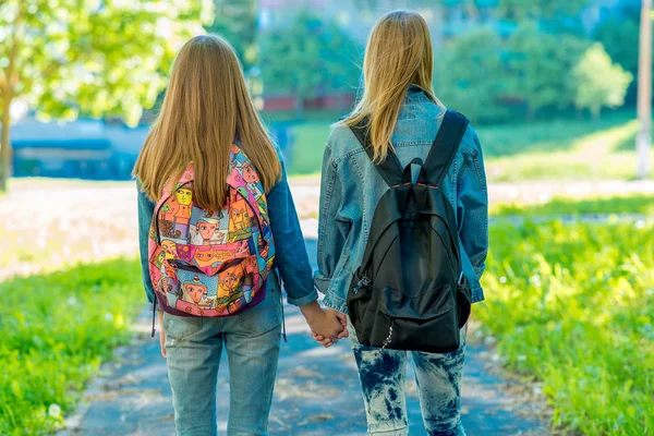 Deux copines écolière. L'été dans la nature. Les filles se tiennent la main. Vue de derrière. Il rentre chez lui après l'école. Le concept d'amitié. Promenade dans le parc . — Photo