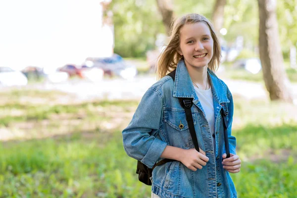 Uma adolescente no verão no parque. Sorrindo feliz depois da escola. Na natureza atrás da mochila. Espaço livre para texto . — Fotografia de Stock