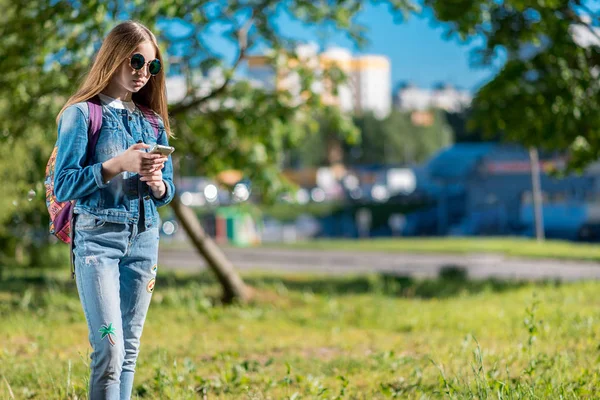 Gadis kecil sekolahan. Musim panas di taman alam setelah sekolah. Menulis pesan smartphone. Ruang kosong untuk teks . — Stok Foto