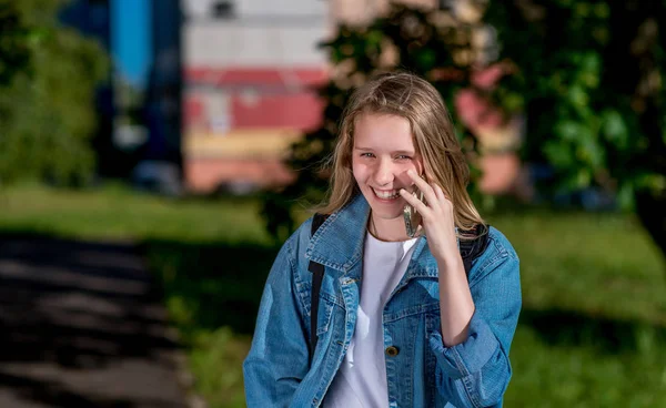 Happy smiling child. In the summer park in nature. Girl schoolgirl is calling by phone. Emotions of joy and pleasure. The concept of positive life. — Stock Photo, Image