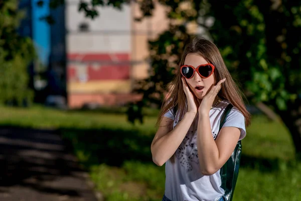 Девочка школьница летом в городе. В очках в форме сердца за рюкзаком. Счастливой улыбки. Концепция неожиданного сюрприза. Свободное место для текста . — стоковое фото